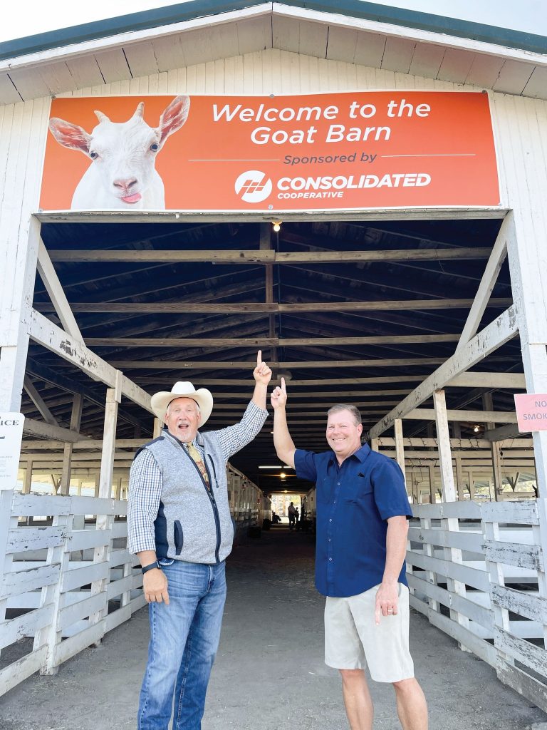 Two consolidated employees stand under the Consolidated sign on the 4-H Goat Barn at the Delaware County Fair